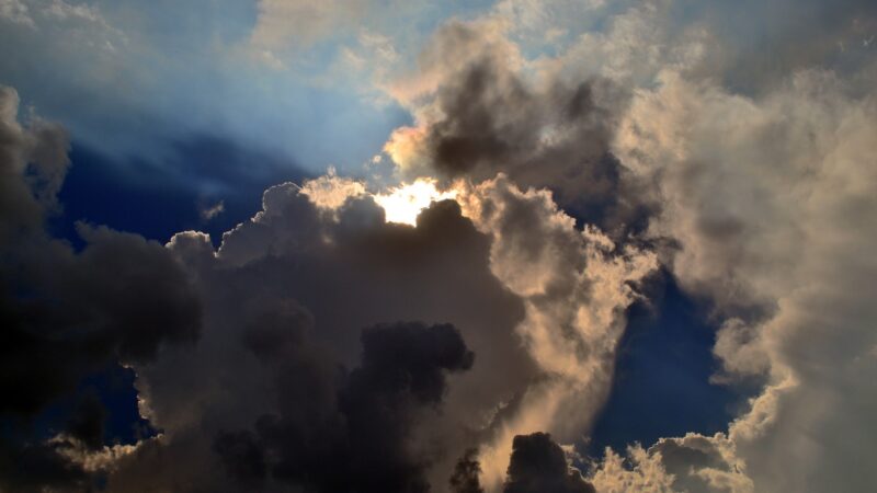 Dramatic cloudy sky with sun rays peeking through dark clouds, creating a stunning natural contrast and light effect.
