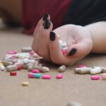 Hand with black nails amidst scattered colorful pills on surface.