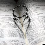 Open Bible with crown of thorns casting heart-shaped shadow, symbolizing love and sacrifice.