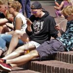 Young adults sitting outside using smartphones, enjoying sunny weather.