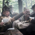 Medieval men in intense confrontation, one in fur and metal headgear, others gesturing and holding papers in a forest setting.