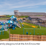 Colorful playground with slides and swings at Ark Encounter, with ark structure in background, on a sunny day.