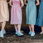 Four women in colorful gingham dresses and sneakers, standing side by side outdoors, showcasing summer fashion.