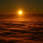 Sunrise over a sea of clouds with a warm glow, creating a serene and majestic skyscape.