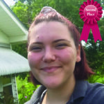 Smiling person outdoors with a second-place ribbon in the corner, green garden background.