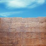 Ancient stone wall against blue sky with scattered clouds, showcasing historical architecture and clear weather.