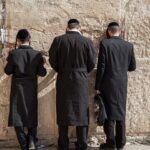 Men praying at the Wailing Wall in Jerusalem, wearing traditional black clothing and hats.