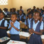 Children in uniform clapping in a classroom, expressing enthusiasm for learning and education.