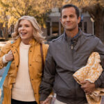 Smiling couple walking hand in hand on a sunny autumn day, holding a blanket and bag.