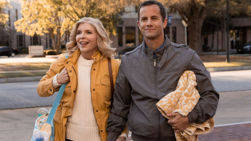 Smiling couple walking hand in hand on a sunny autumn day, holding a blanket and bag.