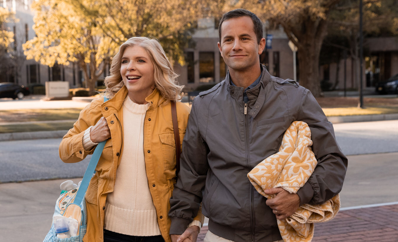 Smiling couple walking hand in hand on a sunny autumn day, holding a blanket and bag.