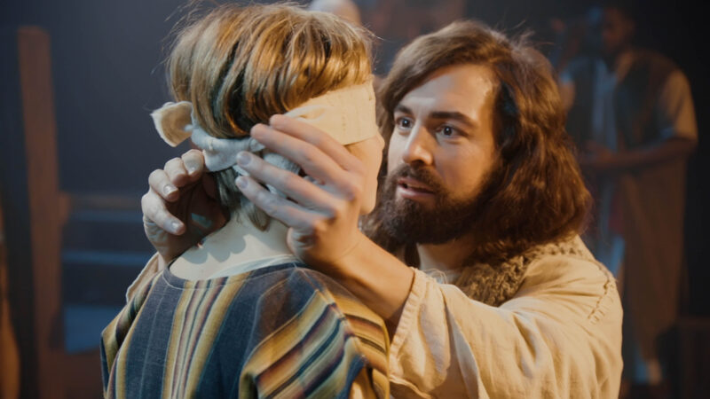 Man with beard tenderly adjusts bandage on another person's head, creating a scene of care and empathy.