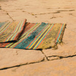 Colorful woven rug on rustic stone pathway outdoors in warm lighting.
