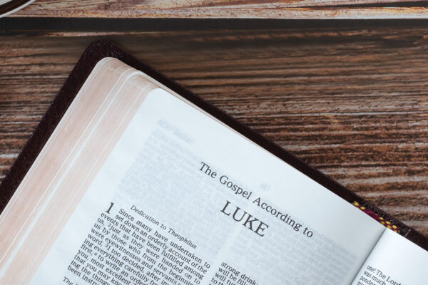 Open holy bible book Luke gospel with coffee cup on wooden background, copy space, top view