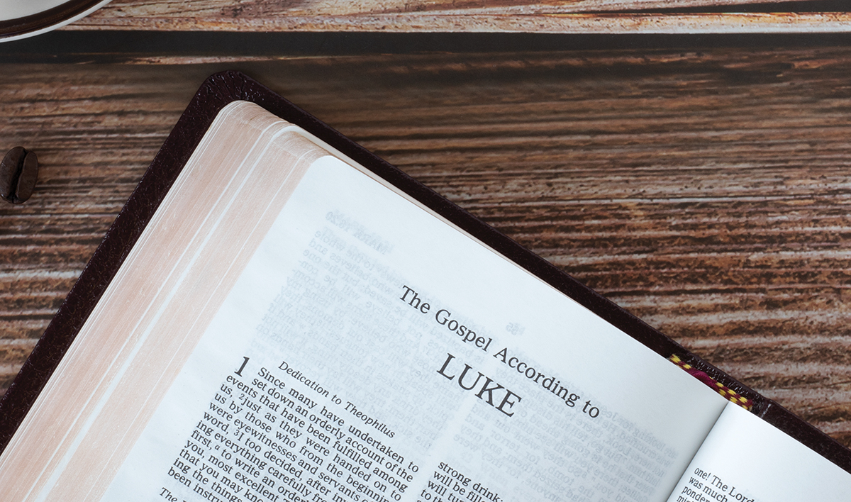 Open holy bible book Luke gospel with coffee cup on wooden background, copy space, top view