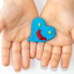 kid mother woman hands with red clay plasticine hearts shape in palm.many colored hearts on table blue yellow colour smiley face emoticon